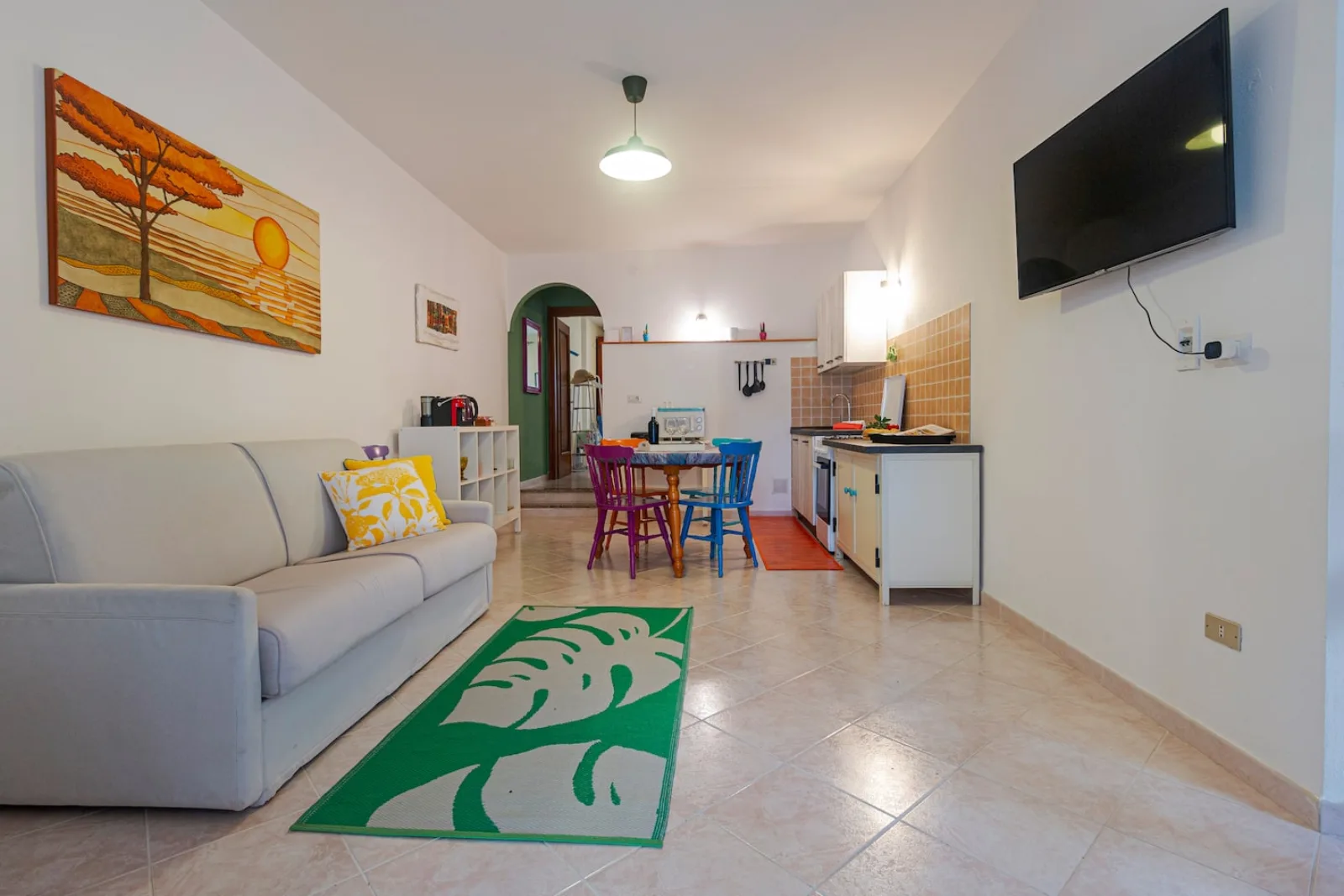 Zona giorno open space di Casa Anita con divano, cucina e tavolo da pranzo colorato.