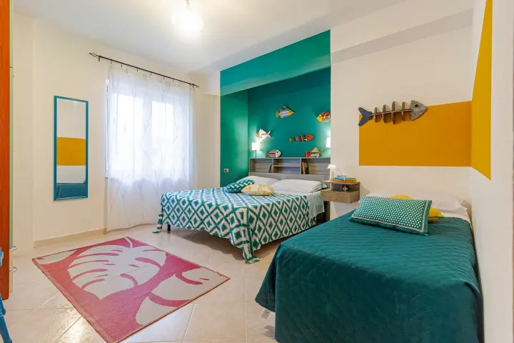 Camera di Casa Anita con letto matrimoniale e letto singolo, parete turchese e dettagli gialli.